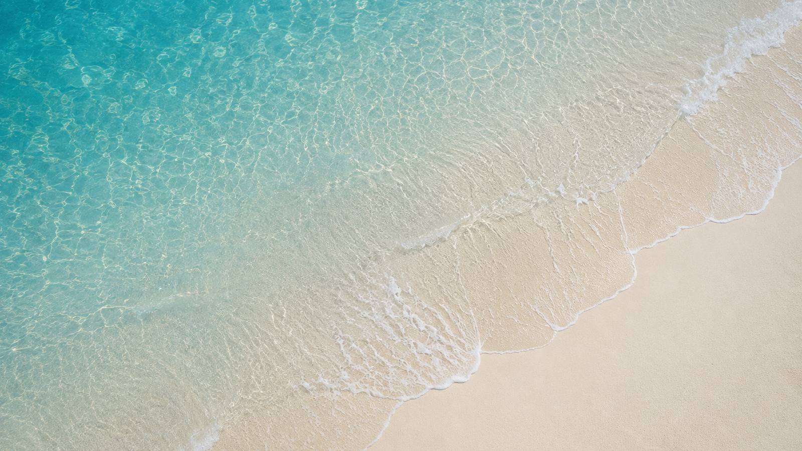 A shoreline seen from above, turquoise water meeting white sand