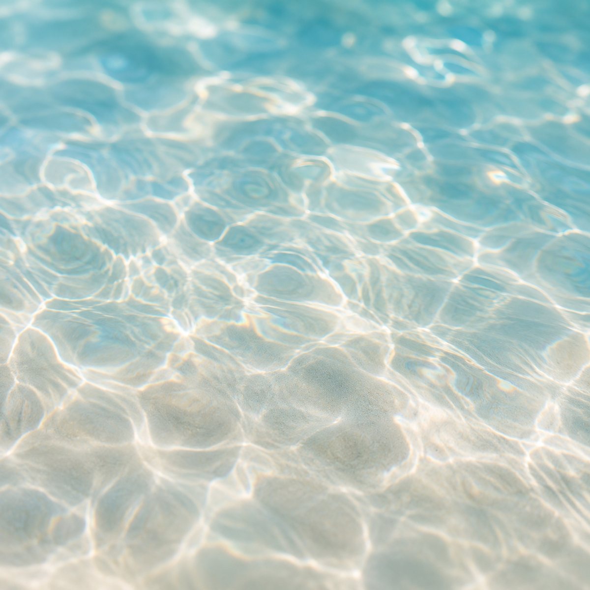 Sunlight rippling across clear shallow water over pale sand